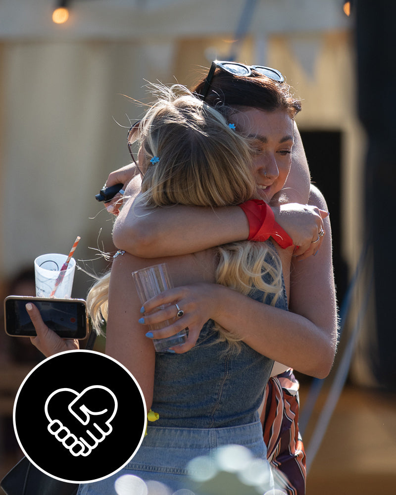 two female employees smiling and hugging with drinks in their hands 
