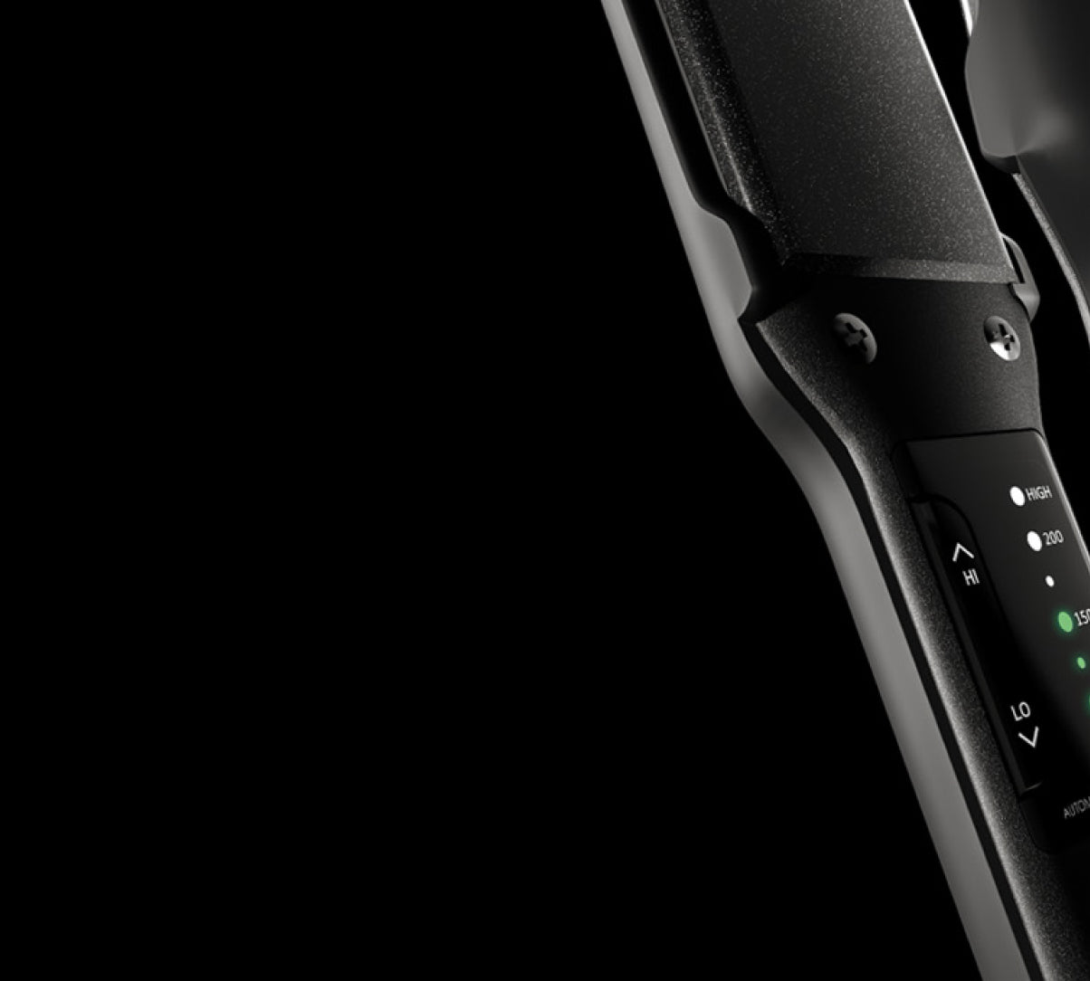 Cropped close up of a black hair straightener and black hair dryer on the right side of a black background.