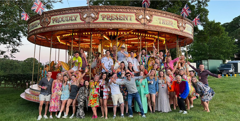 company photo of all the employees at the CLOUD NINE carnival with a horse carousel in the background